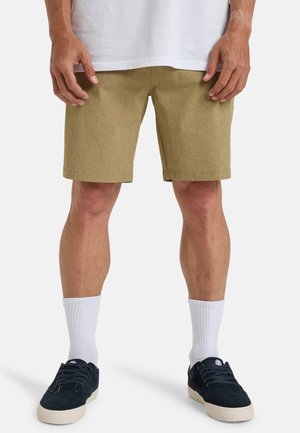 Beige korte broek van een gestructureerde stof, net boven de knieën vallend, gecombineerd met witte crew-sokken en donkere sneakers. Casual pasvorm en ontwerp.
