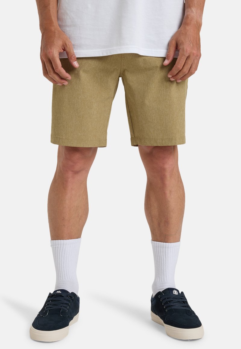 Tan shorts with a textured fabric, falling just above the knees, paired with white crew socks and dark sneakers. Casual fit and design.
