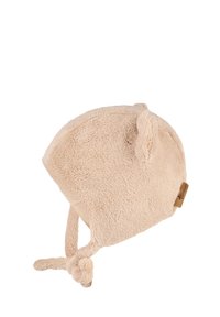 Light beige fleece hat with ear accents, a round shape, and ties with pom-poms. Features a small leather tag on the side. Soft texture.