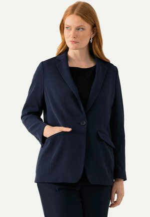 Blazer marine, design ajusté, fermeture à un bouton, deux poches avant, texture de tissu lisse, coupe slim, porté avec un haut noir.