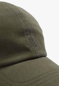 Oliven grøn cap lavet af bomulds twill, med en broderet dødningehovede og korsede knogler detalje på siden. Bøjet skygge og tekstureret stof.
