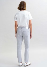 Lichtgrijze slim-fit broek van katoen, met minimale stiksels en twee achterzakken, gecombineerd met een wit t-shirt en witte sneakers.