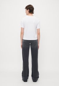 T-shirt bianco a maniche corte abbinato a pantaloni larghi grigi scuri con un orlo leggermente svasato e dettagli di cucitura sottili.