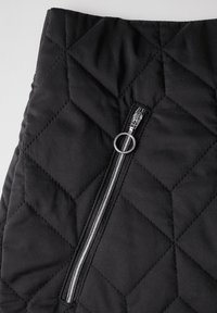 Schwarzer gesteppter Stoff mit Rautenmuster; verfügt über einen Reißverschluss mit einem metallischen Zugband und einem runden Ringakzent in der Nähe der Naht.