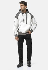 Kapuzensweatshirt mit weißem Körper, grauen Akzenten und seitlichen Paspeln; kombiniert mit schwarzer Hose und dunklen Schuhen. Glatte Textur, lockere Passform.