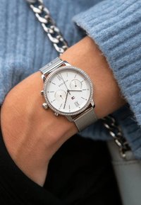 Orologio argento con quadrante bianco, cinturino in rete metallica e funzioni cronografiche; adornato con una ghiera di piccole cristalli.