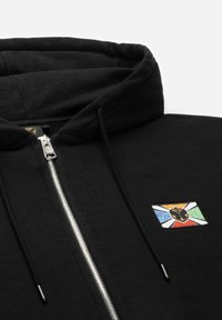 Zwarte zip-up hoodie met een metalen rits. Bevat een multicolore patch met een leeuwenembleem en abstracte patronen op het linkse borstgebied.