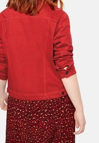 Rød denimjakke med oprollende ærmer, der har en knapdetalje. Kombineret med en rød leopardmønstret nederdel, der viser en dristig kontrast i mønstre.