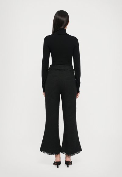 Must mustärkas turtleneck-särgi paaritud tekstuursete mustade flared-pükste juurde, millel on frantsiäärist ääred ja sobiv vöökoht. Riietusel on sujuv ja voolujooneline siluett.