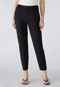Black tailored trousers with a slim fit, featuring side pockets, a flat front, and a smooth woven texture. Styled with a casual top and sandals.