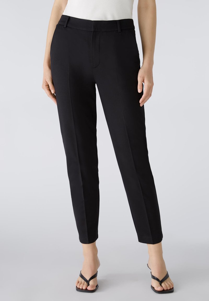 Black tailored trousers with a slim fit, featuring side pockets, a flat front, and a smooth woven texture. Styled with a casual top and sandals.