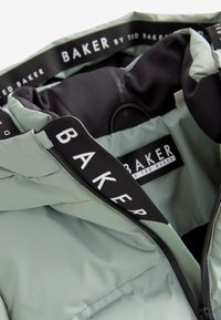Lichtgroene jas met zwarte binnenkant, met zwarte ritstap en witte "BAKER by Ted Baker"-branding op de kraag en binnenlabel.