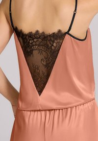 Brzoskwiniowa satynowa odzież z głębokim dekoltem V z czarnymi koronkowymi detalami. Regulowane czarne ramiączka oraz marszczona talia nadają jej struktury.