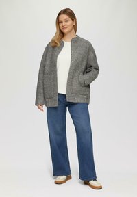 Grijze, gestructureerde jas met een ronde halslijn, knoopsluiting en zijzakken. Draagt over een witte top en gecombineerd met blauwe jeans.