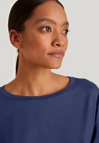 Navyblauwe sweatshirt met een brede halslijn, zachte textuur en zichtbare stikseldetails. Casual pasvorm, past goed bij verschillende outfits.