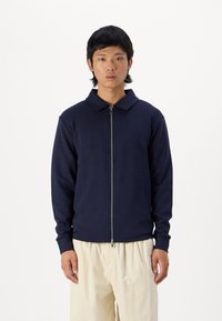 Navy blue zip-up jacket with a collar, made of smooth fabric; features long sleeves and a fitted design.