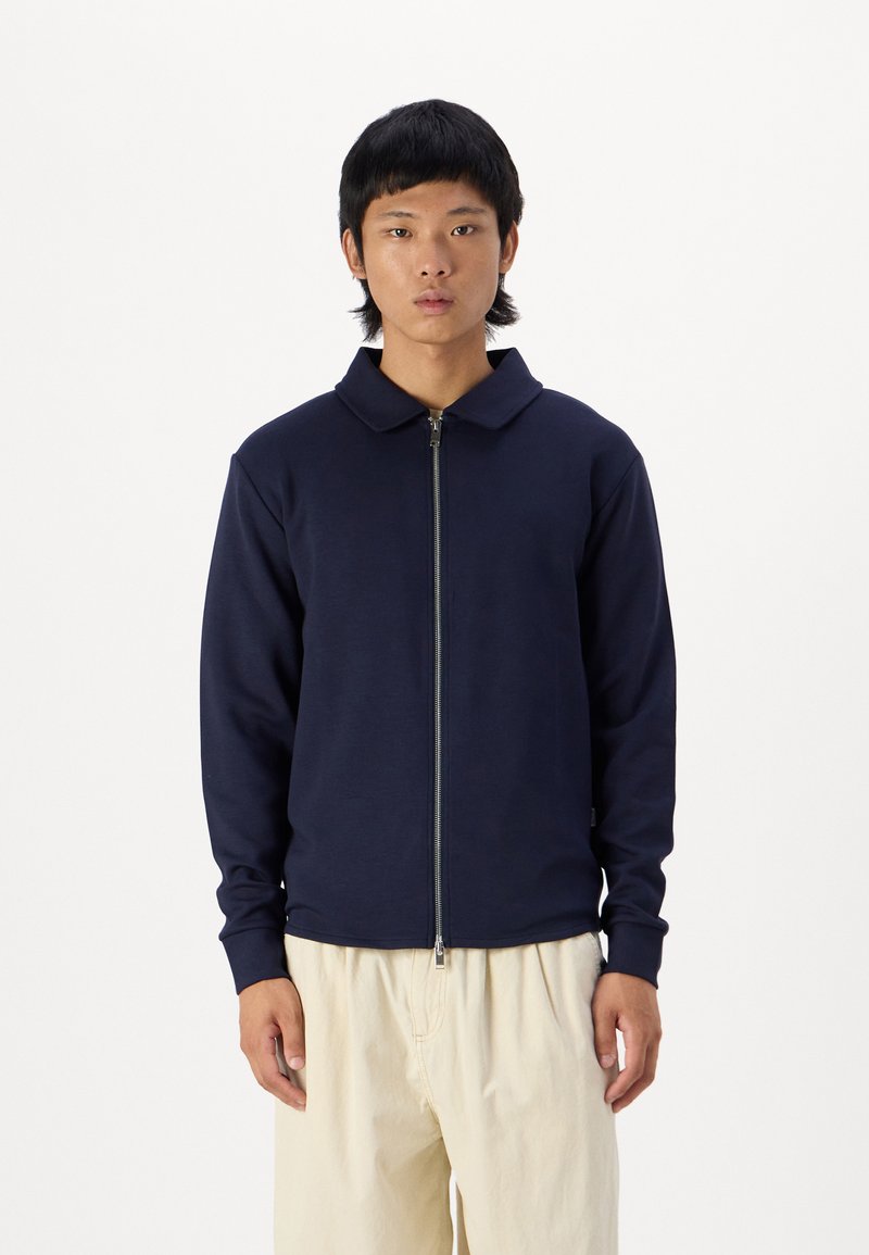 Navy blue zip-up jacket with a collar, made of smooth fabric; features long sleeves and a fitted design.