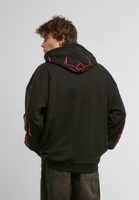 Sudadera negra con un diseño gráfico rojo en la espalda y las mangas, fabricada con un material suave, de corte holgado y con capucha ajustable.