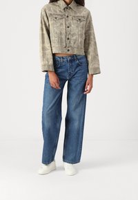 Afklippet, lysegrøn denimjakke med et subtilt bladmønster, parret med løstsiddende blå jeans og hvide sneakers.