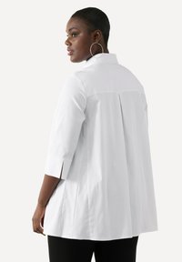 Camicia bianca con colletto, maniche a tre quarti, dettaglio di pieghe sul retro e vestibilità rilassata. Tessuto morbido e leggero.