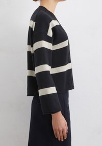 Schwarz-cream gestreifter Cardigan mit einem cropped Design, langen Ärmeln und einer Knopfverschluss. Strukturierte Strickware und lockere Passform.