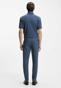 Granatowa koszulka polo w parze z dopasowanymi spodniami. Gładka tekstura, krótkie rękawy, kołnierzyk i proste nogawki. Wygląd dopełniają skórzane buty.