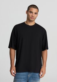 T-shirt nera oversize in cotone morbido con scollatura rotonda e maniche corte, abbinata a jeans chiari strappati. Design semplice.