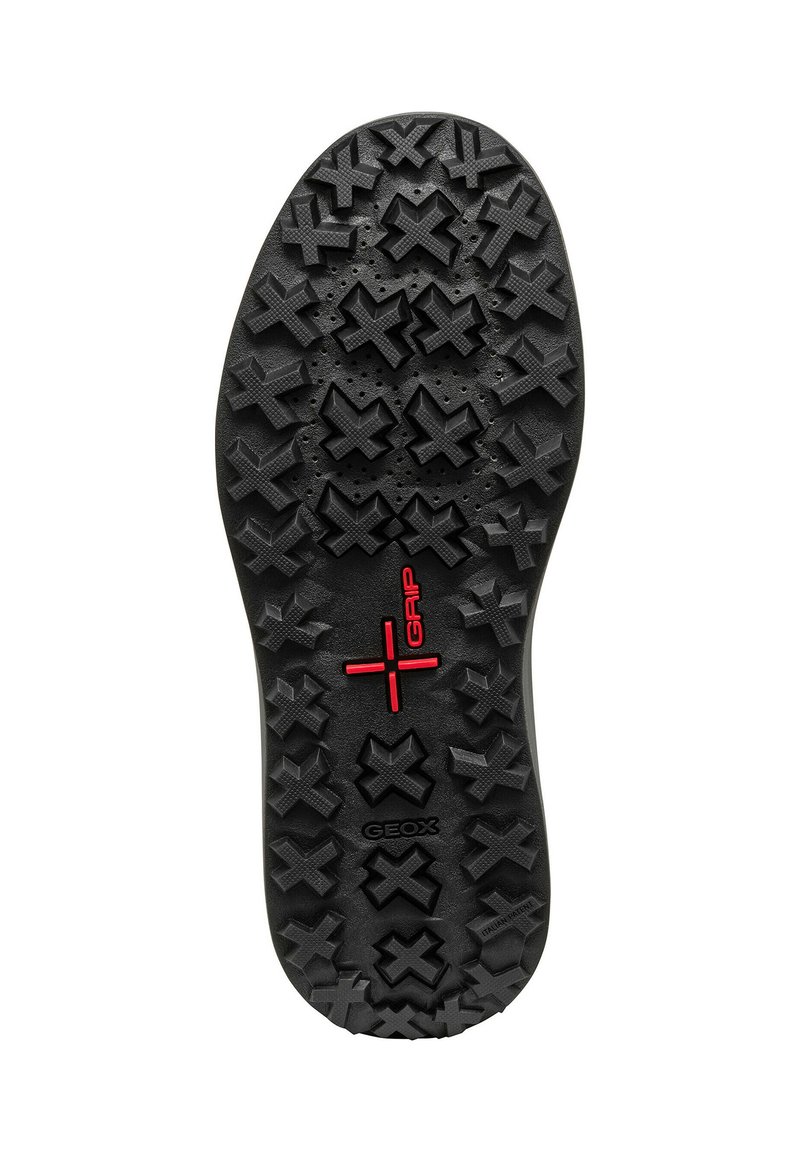 Semelle de sneaker noire présentant un motif en caoutchouc texturé avec des grips en forme de croix et un logo "Grip" rouge. Durable et conçu pour offrir une bonne traction.