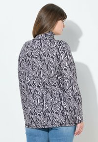 Chemise à manches longues présentant un motif de feuilles noir et blanc, un col montant et une coupe décontractée. Fabriquée en tissu doux et texturé.