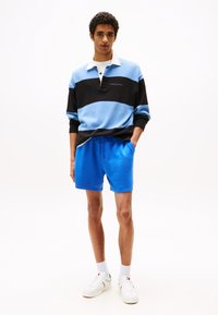 Blue and black striped pullover with a collar, paired with blue shorts. Model wears white sneakers and textured white socks. Simple design.