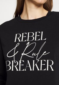 Felpa nera con testo bianco che legge "REBEL & Rule BREAKER." Tessuto liscio, collo tondo e maniche lunghe.