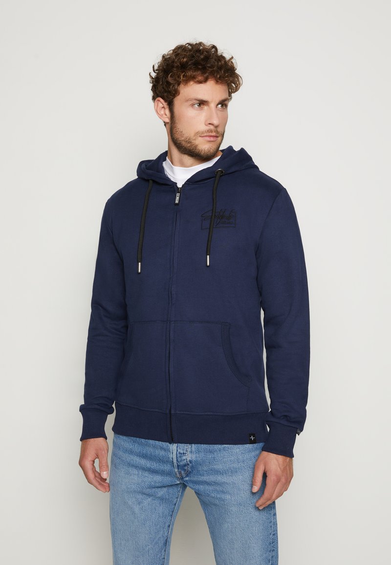 Marineblaue Zip-Up Kapuzenjacke aus weichem Baumwollmix, mit einer Fronttasche, verstellbarem Kordelzug an der Kapuze und kontrastierenden Nähdetails.