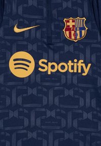 Marinblå tröja tillverkad av lättviktig tyg, med en texturerad mönster, Nike-logotyp, FC Barcelona-emblem och guld Spotify-märkning.