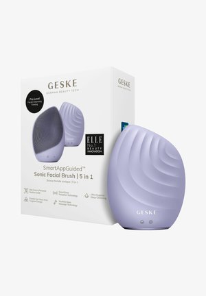 Sonic ansigtbørste i lavendel med buet form, tekstureret overflade og to knapper. Begge dele præsenteres i en hvid æske, der viser produktdetaljer.