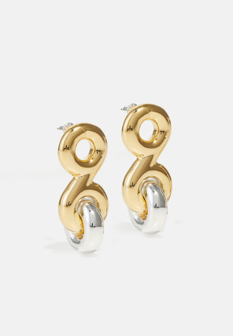 Cercei din metal aurit și argintie cu un design unic și răsucit, prezentând accente circulare și un finisaj lucios.