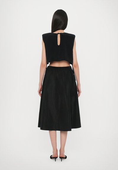 Zwarte crop top met een open rug en strikdetails, gecombineerd met een vloeiende zwarte rok. Beide stukken zijn gemaakt van soepele stoffen en hebben een minimalistisch ontwerp.