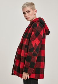 Rdeča in črna karirasta flis jakna s kapuco, z zadrgo in mehko, teksturirano površino. Pravokotna silhueta z velikim prileganjem.