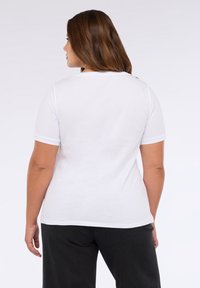 Camiseta blanca de manga corta con cuello redondo, hecha de algodón suave, con un corte holgado y un diseño sencillo, combinada con jeans oscuros.