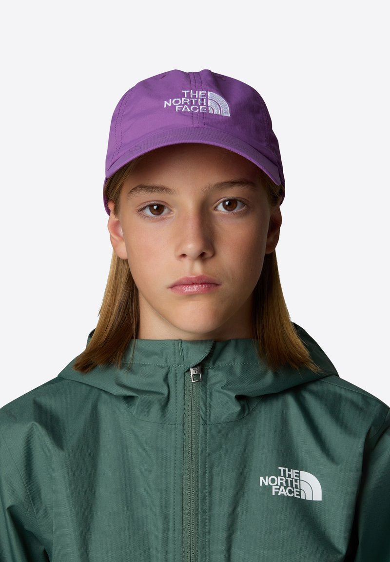 Cappello viola con logo bianco, indossato con una giacca verde con zip frontale e cappuccio. Il tessuto sembra liscio e leggero.