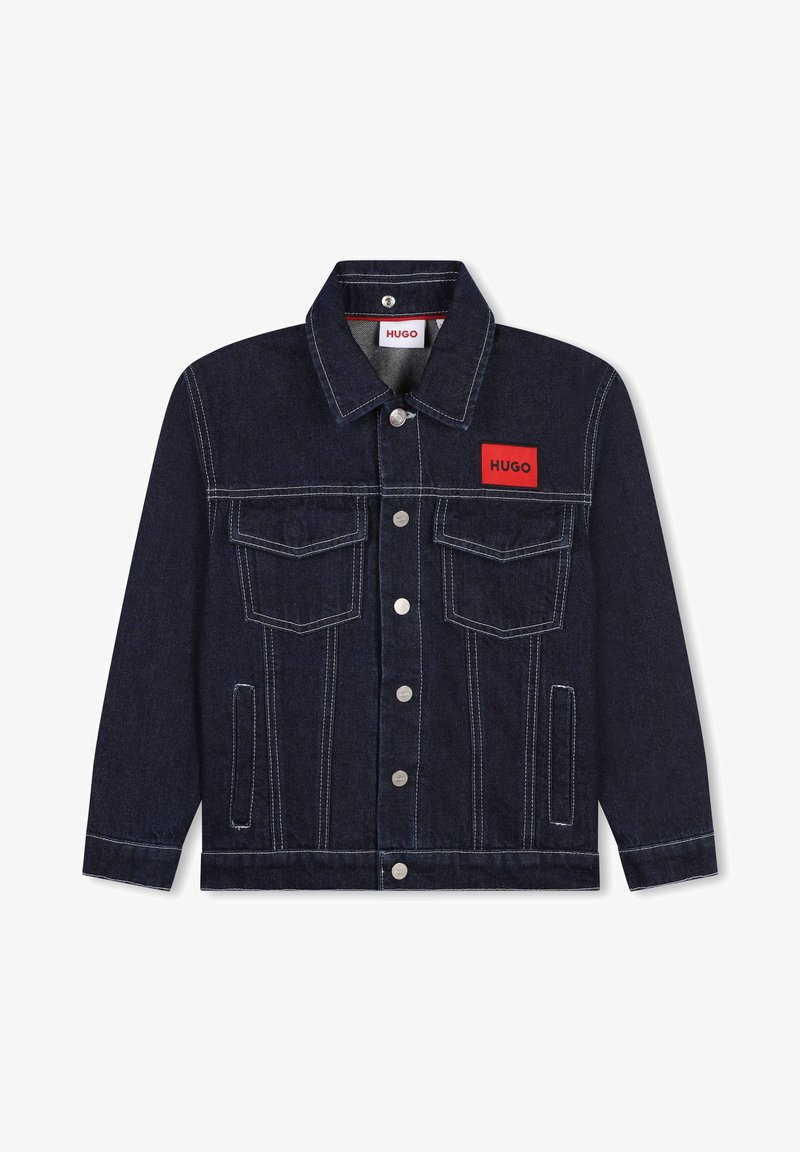 Tumši zila džinsu jaka ar baltu šuvju. Iespējas ietver sarkanu logotipa aploksni, divas krūšu kabatas un metāla pogas.