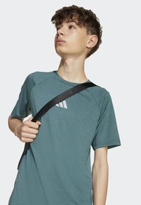 Tyrkysové športové tričko s textúrovaným povrchom, krátkymi rukávmi a okrúhlym výstrihom, s bielym logom na hrudi.