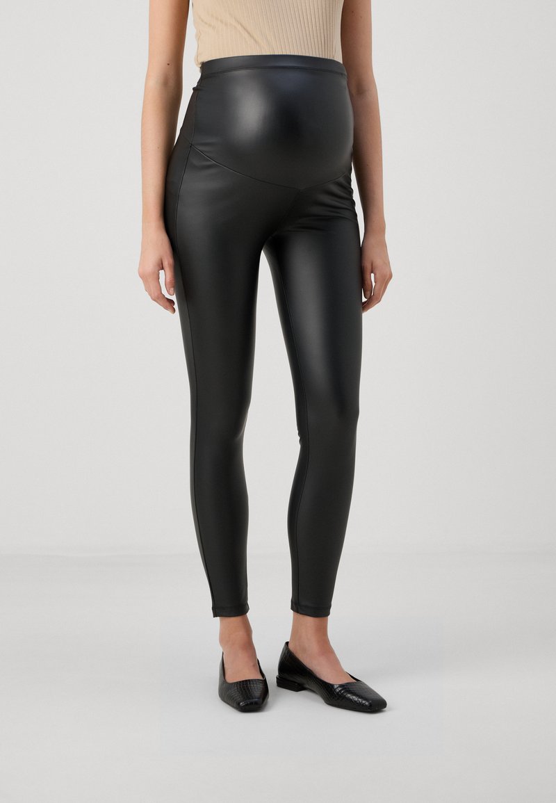 Graviditetstights i svart konstläder, högmidjad design, slät textur, åtsittande silhuett, i kombination med svarta ballerinaliknande skor, minimalistisk stil.