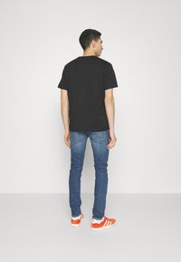Camiseta de algodón negra combinada con jeans azules y zapatillas naranja y blancas. La camiseta tiene mangas cortas y un diseño de corte recto.