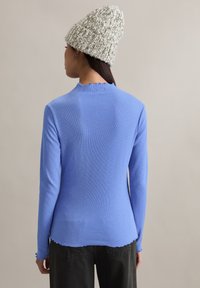 Langärmeliges hellblaues Oberteil mit gerippter Struktur und gewelltem Ausschnitt, kombiniert mit einer grob gestrickten cremefarbenen Mütze.