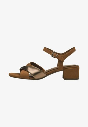 Braune Wildleder-Blockabsatzsandalen mit überkreuzten metallischen Riemen, verstellbarem Knöchelriemen und einer strukturierten Innensohle für Komfort.