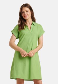 Grünes Kleid mit umgeschlagenen Ärmeln, gefertigt aus leichtem Stoff. Das Design ist einfach und hat einen V-Ausschnitt.