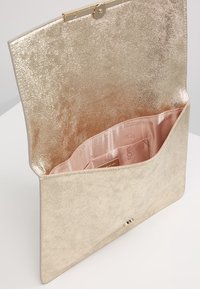 Gold metallic clutch bag with a textured surface. Interior is lined in soft pink fabric, featuring a small pocket and a clasp closure.