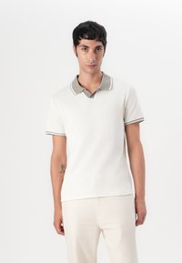 Hellbeige Polo-Shirt mit strukturiertem Stoff, kontrastierendem grauem Kragen und Besatz, kurzen Ärmeln und einem lockeren Schnitt.