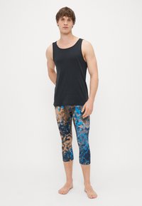 Top sem mangas preto combinado com leggings capri multicoloridas que apresentam um padrão de tie-dye azul e castanho. Tecido macio, design ajustado.