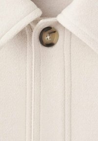 Tissu en mélange de laine beige avec une surface texturée, présentant un grand bouton marron au col et des détails de couture visibles.